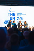 Vier Personen stehen auf der Bühne, sprechen und halten Mikrofone in der Hand. Hinter ihnen ist eine große Leinwand zu sehen, auf der "Chemnitz Kulturhauptstadt Europas 2025" und andere Texte zu lesen sind. Das Publikum schaut von vorne zu.