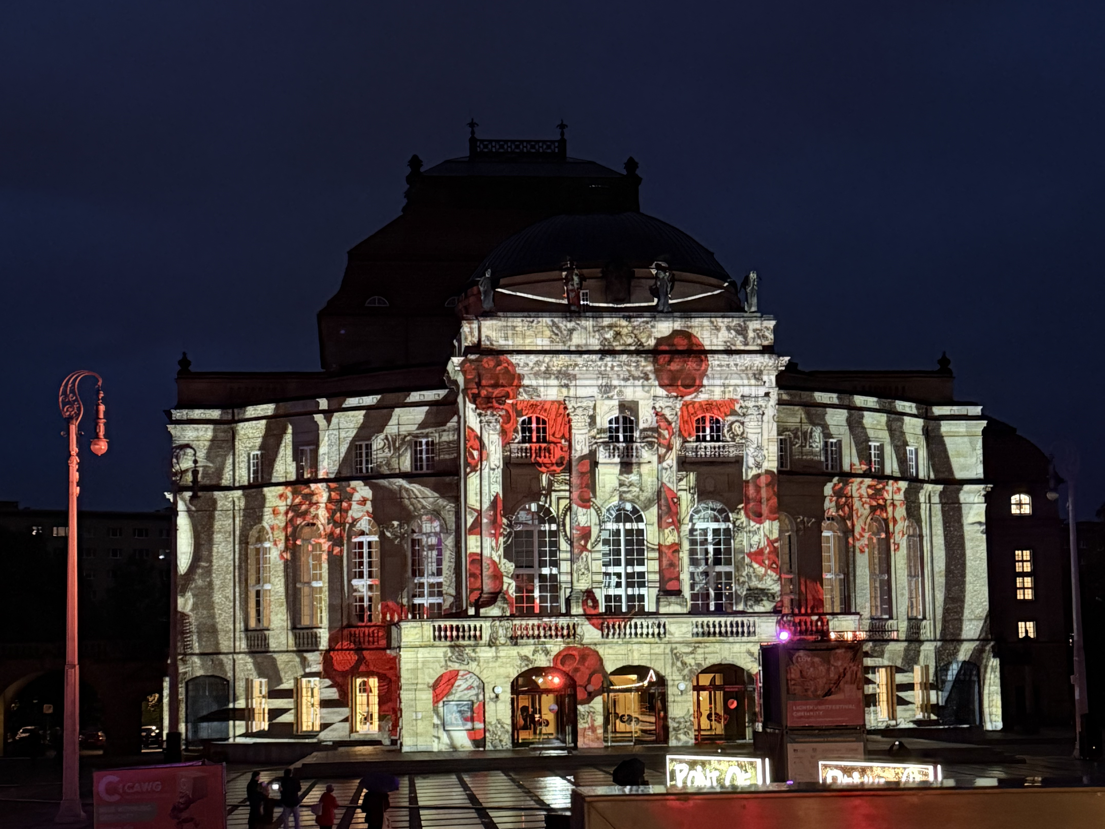 Ein verziertes Gebäude wird nachts mit einer farbenfrohen Projektion aus rotem Mohn und abstrakten Formen auf seiner Fassade beleuchtet, die sich lebhaft vom dunklen Himmel abhebt.